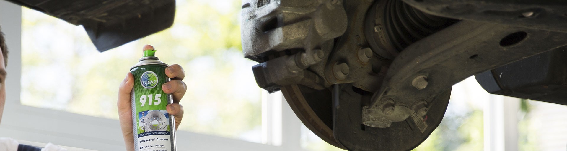 Person points a green spray can towards a dirty brake of a lifted car