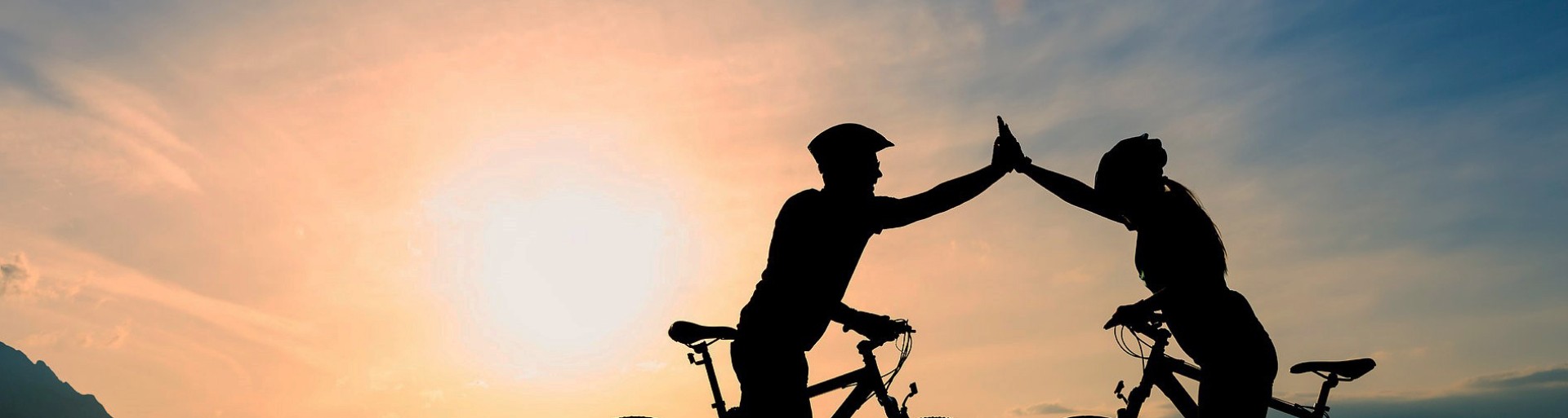 Two cyclists with raised arms with light shining towards the viewer